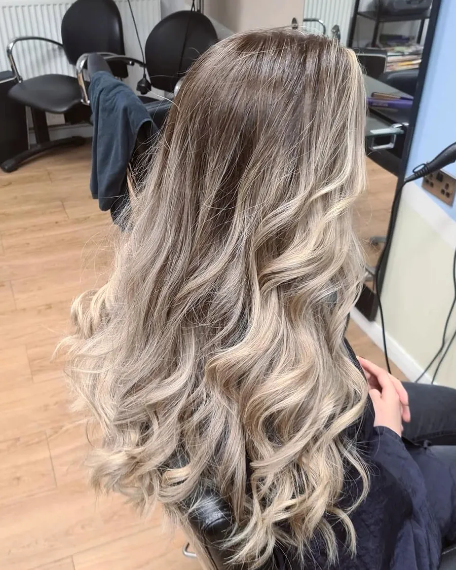 Long hair blended from a natural brown root into cool, creamy blonde lengths, finished in soft glamour waves.