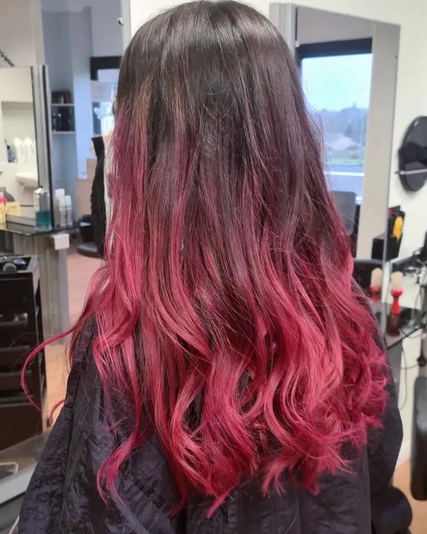 Long dark brown hair melting into vivid raspberry-pink ends, finished in loose waves.