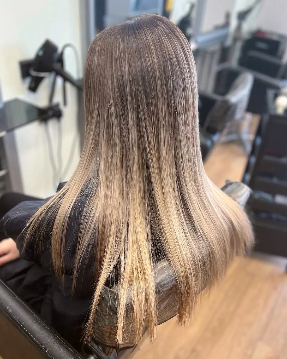 Long, sleek straight hair with a soft brown root fading into sandy blonde ends, cut in a gentle curve across the back.