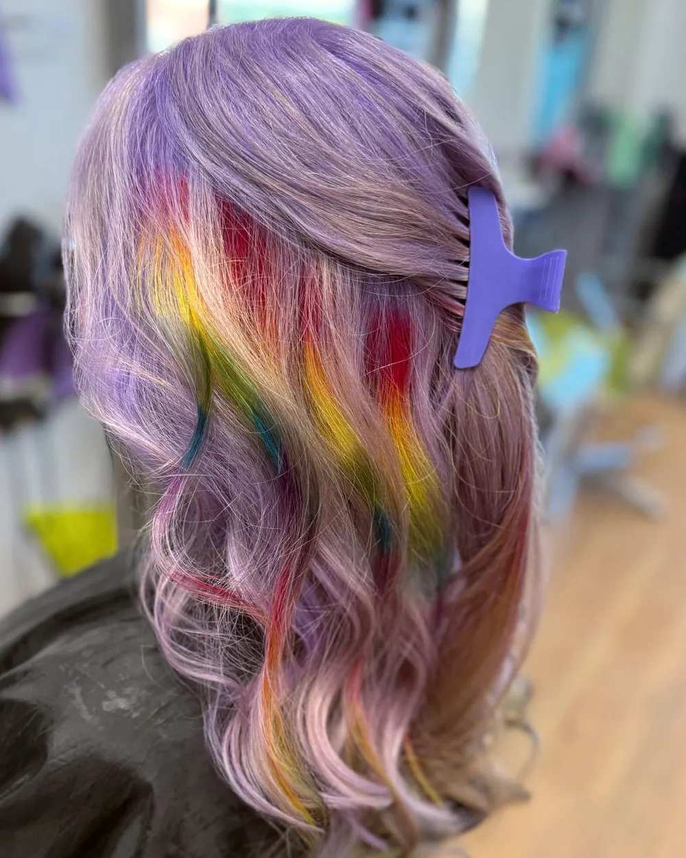 Pastel lilac hair with ribbons of red, yellow, green and teal through the lengths, finished in loose waves.