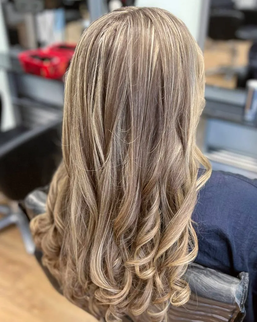 Long hair with fine blonde highlights through a light brown base, set in full, bouncy curls.