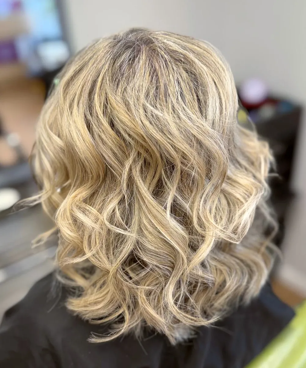 Shoulder-length blonde hair with a softly shadowed root and bright highlights, set in loose, tousled waves.